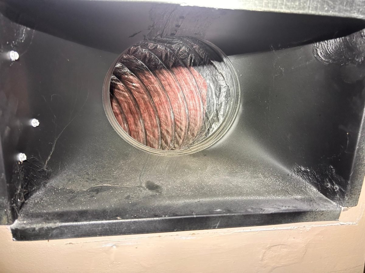 Dusty wall vent boot with flex duct visible behind it