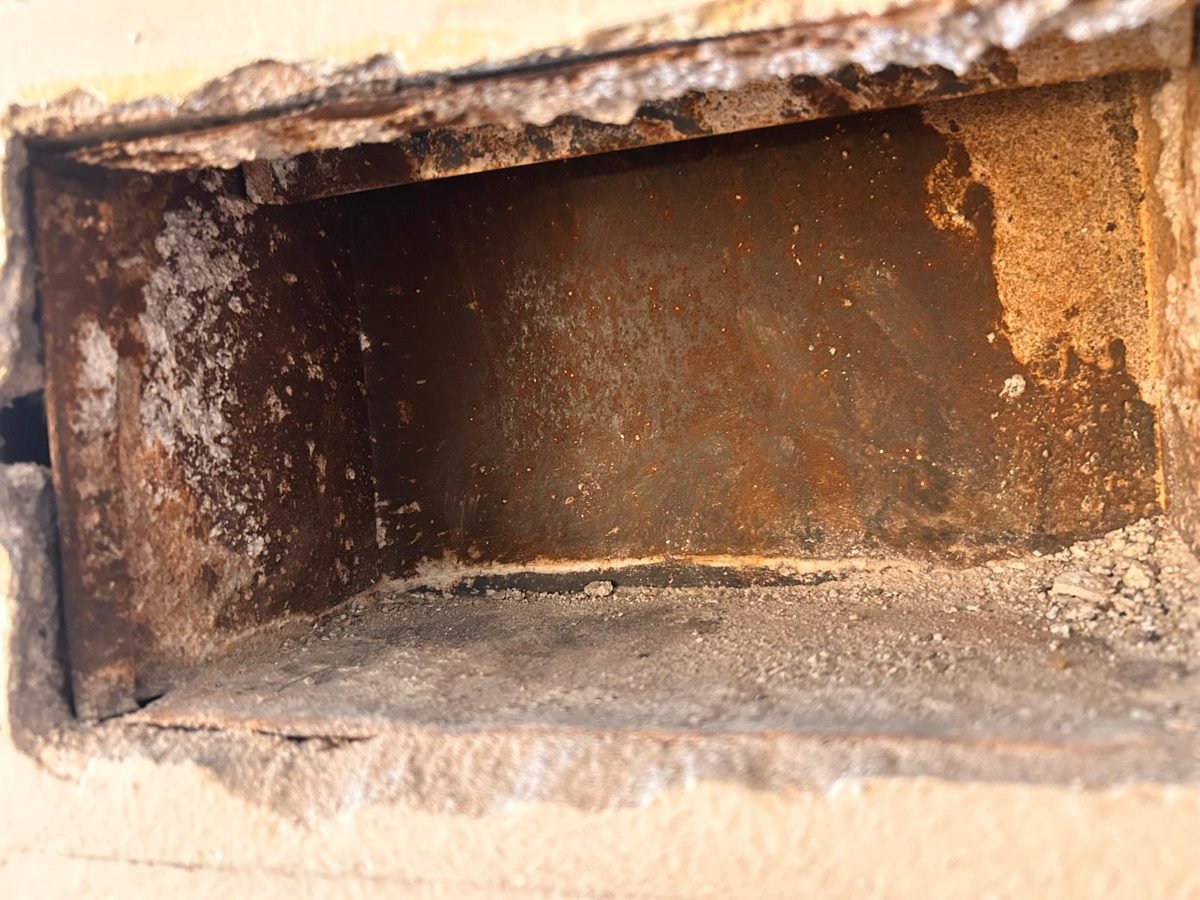 Rusted wall vent boot with debris collected at the bottom